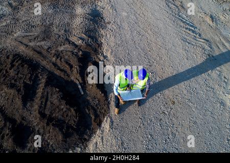 Aerial image of two engineers with helmets and vests looking at blueprints on construction site Stock Photo