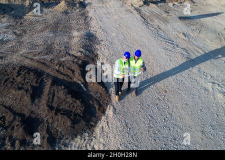 Aerial image of two engineers with helmets and vests looking at blueprints on construction site Stock Photo