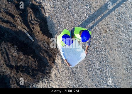 Aerial image of two engineers with helmets and vests looking at blueprints on construction site Stock Photo