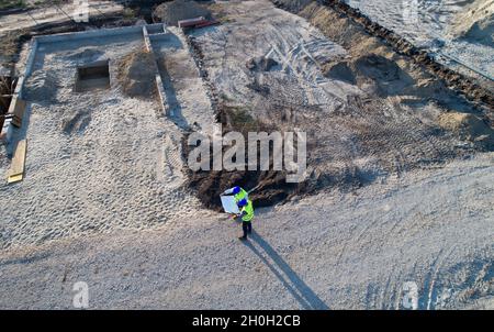 Aerial image of two engineers with helmets and vests looking at blueprints on construction site Stock Photo
