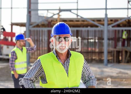 Portrait of senior engineer with helmet and vest in front of metal structure on building site Stock Photo