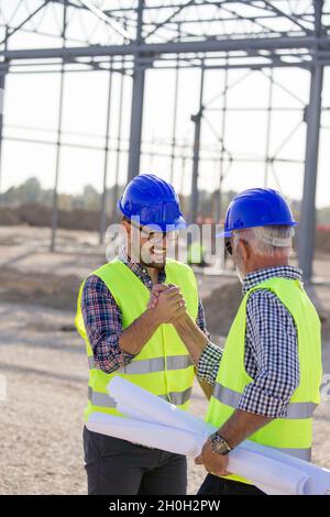 Two engineers shaking hands on building site with metal construction in background Stock Photo