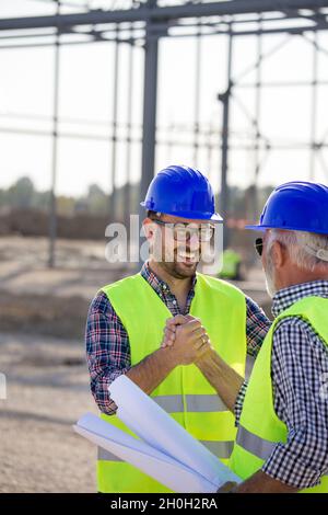 Two engineers shaking hands on building site with metal construction in background Stock Photo
