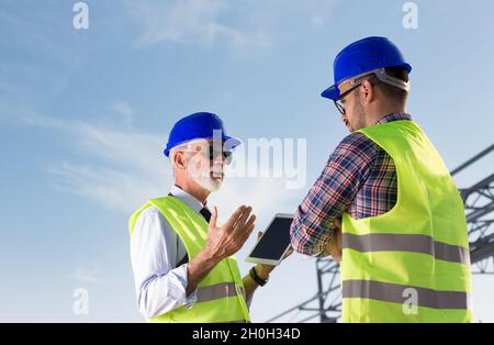 Senior engineer and construction worker talking in front of metal structure at building site Stock Photo