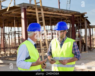 Two satisfied engineers with tablet talking at building site Stock Photo