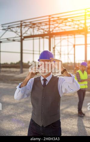 Portrait of foreman with helmet talking on mobile phone in front of metal structure at building site Stock Photo