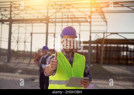 Portrait of satisfied engineer holding tablet and showing thumb up on building site Stock Photo