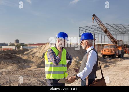 Two engineers with helmets talking at building site in front of metal construction Stock Photo