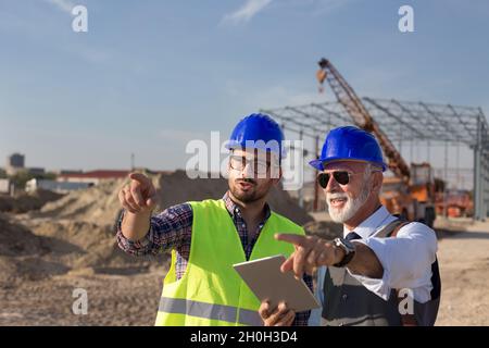 Two satisfied engineers talking at building site with construction structure in background Stock Photo