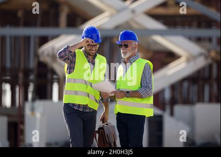 Twp satisfied engineers talking at building site with metal construction in background Stock Photo