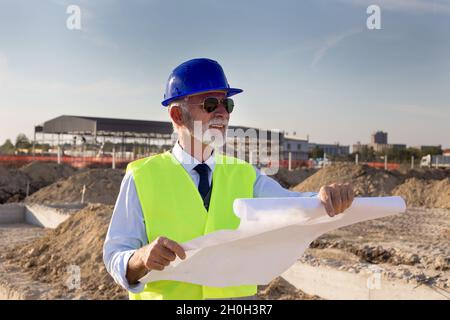 Senior engineer looking at blueprints in front of metal construction at building site Stock Photo