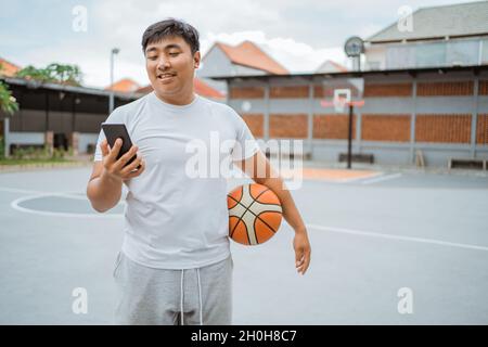a basketball player using a mobile phone while standing holding the ball Stock Photo