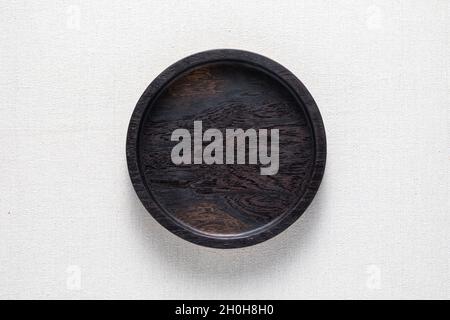 Dark black handmade round wooden plate on burlap. Round tray. Stock Photo