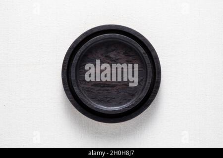 Dark black handmade round wooden plate on burlap. Round tray. Stock Photo