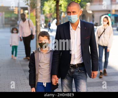 Father with son in protective face mask for spreading of virus disease prevention walking on city street Stock Photo