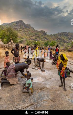 Young girls grinding Sorghum on a rock, Laarim tribe, Boya hills, Eastern Equatoria, South Sudan Stock Photo