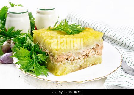 Mashed potato casserole with salmon fillet and lettuce in a plate, kitchen towel, garlic on the background of a light wooden board Stock Photo