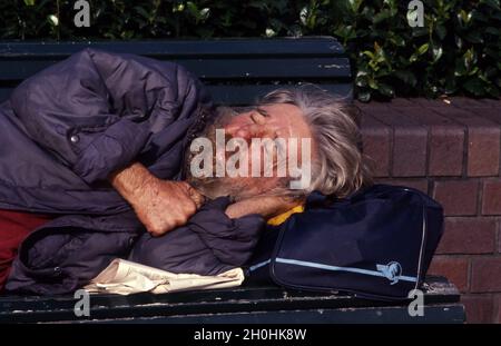AN ELDERLY HOMELESS MAN ASLEEP ON A PARK BENCH WITH HIS HEAD RESTING ON HIS POSSESSIONS. SYDNEY, NEW SOUTH WALES, AUSTRALIA. Stock Photo
