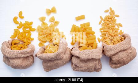 Italian foods concept and menu design . Various kind of Pasta Elbow Macaroni ,Farfalle ,Rigatoni ,gnocco Sardo in hemp sack bags setup on white wooden Stock Photo