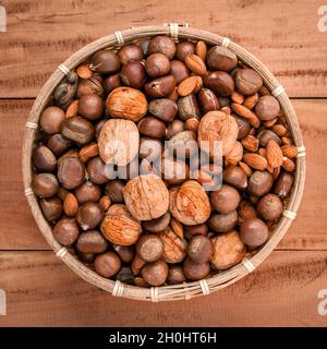 Mixed different kinds of nuts in shells ,cashew, almond, walnut, hazelnut, pistachio, hazelnuts, pecan and  macadamia in the busket on rustic wooden b Stock Photo