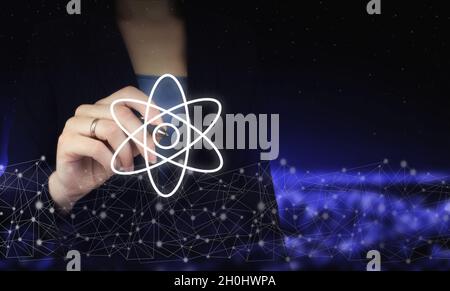 Atom molecule abstract. Hand holding digital graphic pen and drawing digital hologram molecule atom sign on city dark blurred background. Atom molecul Stock Photo