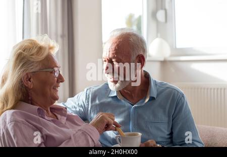 Senior couple sitting on sofa talking and drinking coffee. Loving atmosphere at home Stock Photo