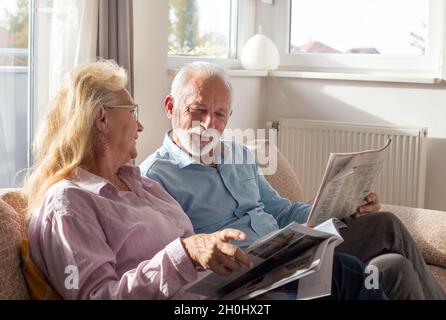 Senior couple reading newspaper and magazine on sofa at home Stock Photo