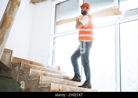 Builder man in hardhat carrying timber on building site, close up . Stock Photo