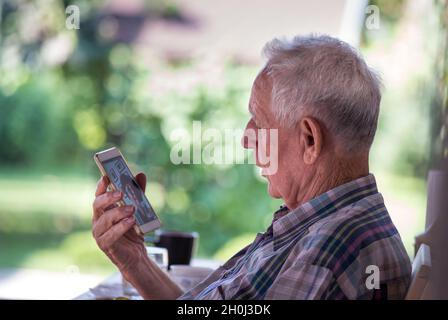 Confused senior man sitting in park and talking on cell phone Stock Photo