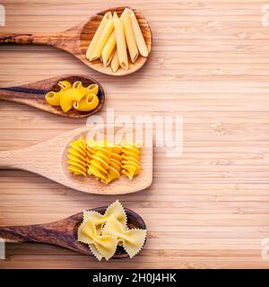 Italian foods concept and menu design. Various kind of Pasta Elbow Macaroni ,Farfalle ,Fusilli  and Penne in wooden spoons setup on bamboo cutting boa Stock Photo