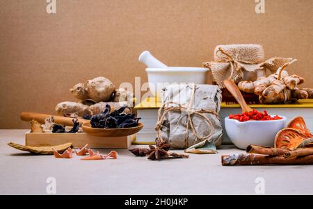 Alternative health care dried various Chinese herbs in wooden box lotus seed and saffron in wooden spoon on medical textbook with mortar on brown back Stock Photo