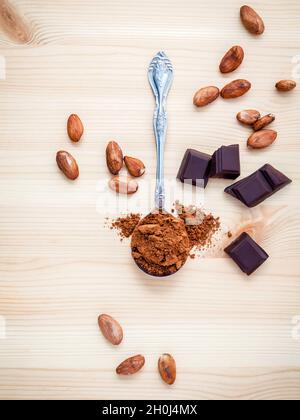 Brown chocolate powder in spoon , Roasted cocoa beans and dark chocolate setup on wooden background. Stock Photo