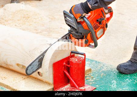 A chainsaw cuts a tree trunk. Men's hands in protective gloves grip the tool firmly. Close-up, copy space. Stock Photo