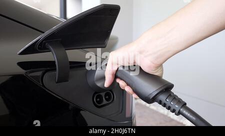 Close-up of an arm inserting an electric car charger into a black electric car. Stock Photo