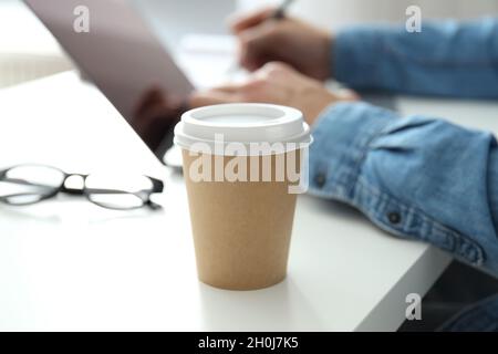 Blank paper cup against young man working on laptop. Stock Photo