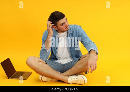 Young man and laptop on yellow background. Stock Photo