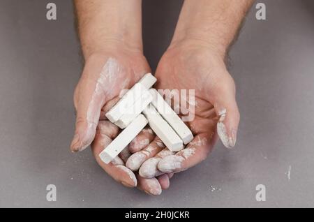 Pieces of white chalk lie in the man's palms against a gray background. The man is holding five rectangular pieces of chalk in his hands. Selective fo Stock Photo