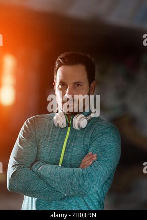 Portrait of attractive satisfied man in sportswear with crossed arms in front of urban colorful background Stock Photo