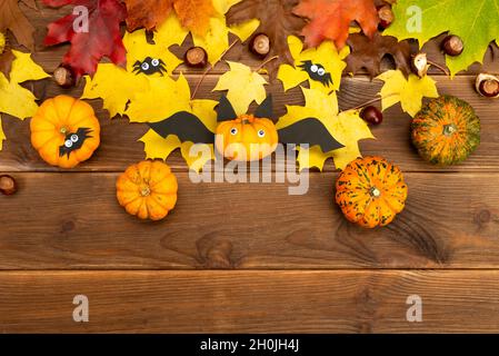 Autumn decor of pumpkin and yellow maple leaves on a wooden background with copy space. DIY pumpkin craft in the shape of a bat. Halloween decor. Stock Photo