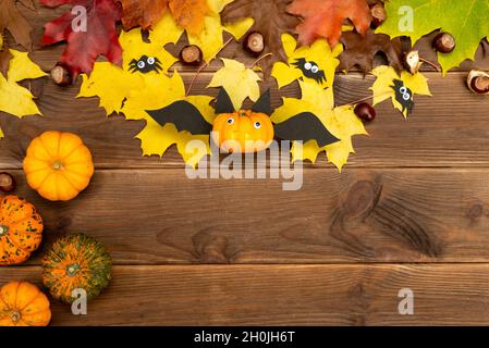 Autumn decor of pumpkin and yellow maple leaves on a wooden background with copy space. DIY pumpkin craft in the shape of a bat. Halloween decor. Stock Photo