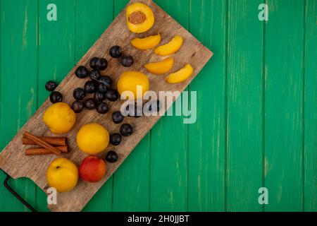 top view of fruits as sliced cut and whole apricots and sloe berries with cinnamon on cutting board on green background with copy space Stock Photo