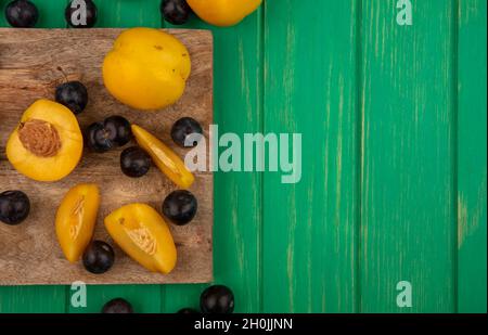 top view of fruits as sliced and whole apricots and sloe berries on cutting board and on green background with copy space Stock Photo