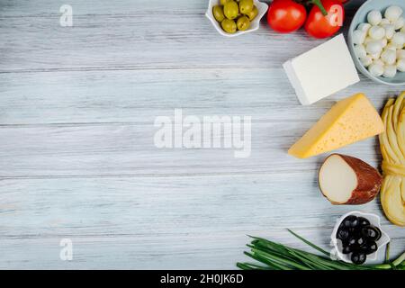 top view of different kinds of cheese with green onion, fresh tomatoes and pickled olives on grey wooden background with copy space Stock Photo