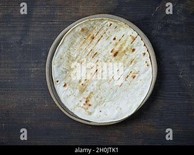 empty tortilla on ceramic plate on black wooden kitchen table, top view Stock Photo
