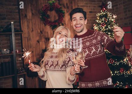 Photo of funny funky husband wife dressed print pullovers enjoying noel drinking wine holding sparkles smiling indoors room home house Stock Photo