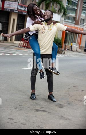 young man carrying his girlfriend on the back and looking at her smiling. Stock Photo