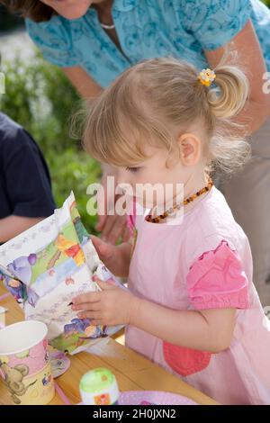 children's birthday party, little girl unwrapping her birthday present Stock Photo