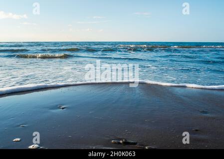 Beautiful wild beach of the Sea of Okhotsk, Sakhalin island, Nevelsk, Russia. Endless sea and clear blue sky. Waves are washed up to the shore. Stock Photo