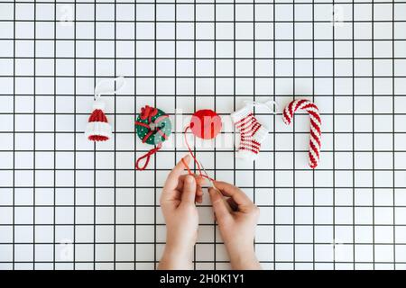 Christmas Knit Toys. Handmade DIY Crochet hat, lollipop, donut and sock and female hand with crochet hook on checkered white background. Christmas Stock Photo
