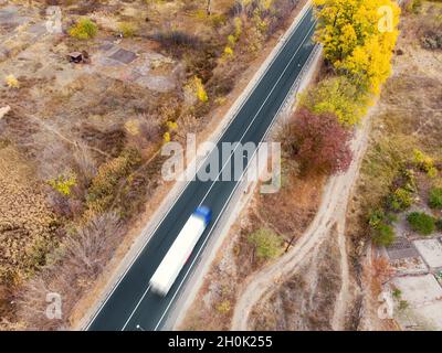 Aerial top view white semi trailer truck delivery shipment cargo courier moving fast on motorway road city urban suburb. Business distribution and Stock Photo